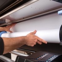 Close-up man hands loading wide format white paper roll on professional printer